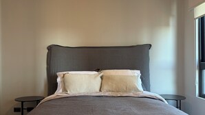 A bedroom with a bed, two bedside tables, a hanging light fixture, and a window. - Valpo Coast Suites · Modern Apartment + Parking + Rooftop (Valparaíso)