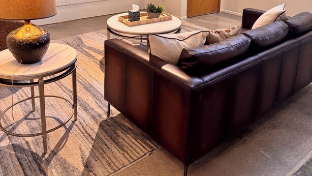 A modern living room with a sofa, a coffee table, a TV, a fireplace, and a kitchen area.