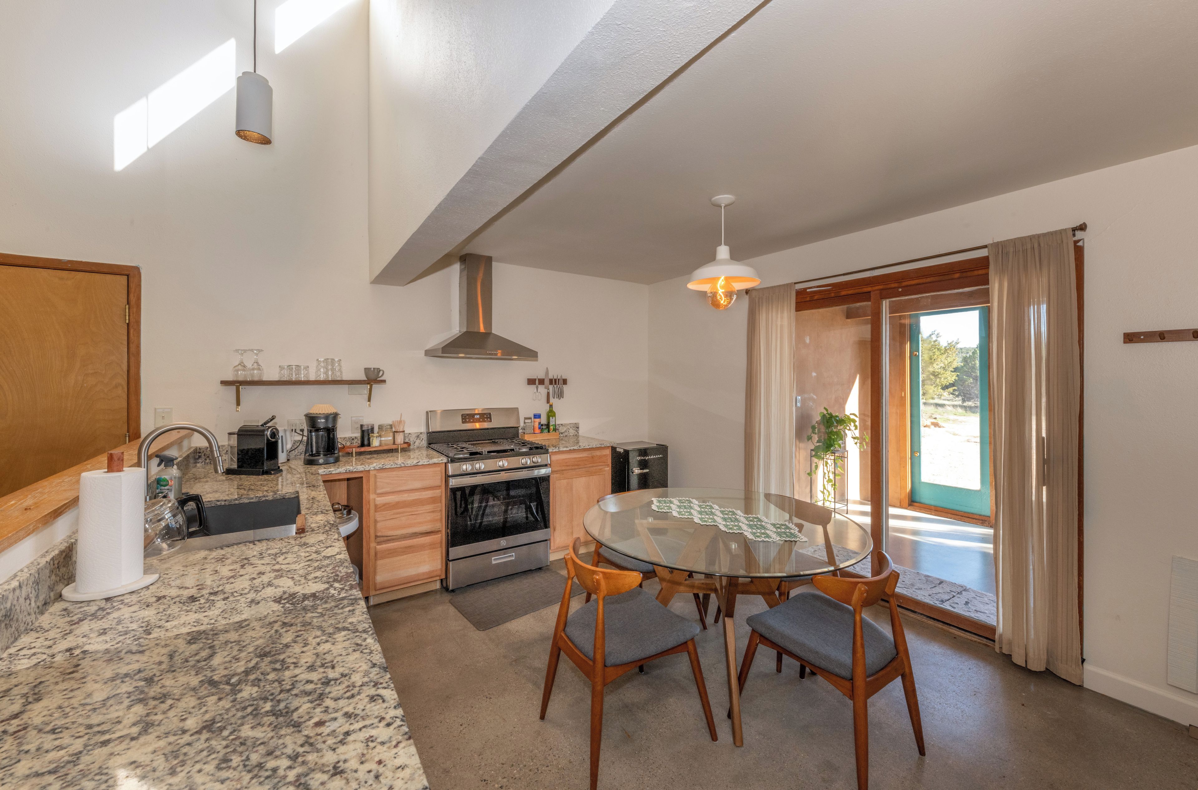 A modern kitchen with granite countertops, stainless steel appliances, and a dining area with a glass table and wooden chairs.