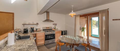 A modern kitchen with granite countertops, stainless steel appliances, and a dining area with a glass table and wooden chairs.