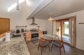 A modern kitchen with granite countertops, stainless steel appliances, and a dining area with a glass table and wooden chairs. - Ranch Retreat near Santa Fe • Indoor Pool, Hot Tub & Big Skies (Lamy)