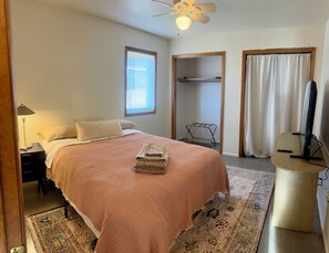 A bedroom with a bed, a nightstand, a ceiling fan, a window with blinds, a wardrobe, a television, and a rug. - Spacious 6-bedroom house on 115 acre ranch in Lamy/Santa Fe (Lamy)