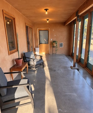 A spacious room with a concrete floor, a wooden ceiling, and large windows. There are two chairs and a small table with a potted plant. - Ranch Retreat near Santa Fe • Indoor Pool, Hot Tub & Big Skies (Lamy)