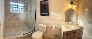 A bathroom with a shower, toilet, sink, and a poster on the wall. - Spacious 6-bedroom house on 115 acre ranch in Lamy/Santa Fe (Lamy)