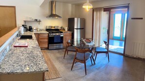 A kitchen with granite countertops, a stove, oven, and a refrigerator. There is a dining table with chairs and a window with a view.