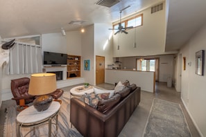 A spacious living room with a leather sofa, a television, and a fireplace. - Ranch Retreat near Santa Fe • Indoor Pool, Hot Tub & Big Skies (Lamy)