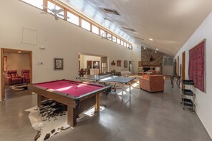 A spacious living area with a pool table, a sofa, and a fireplace. - Ranch Retreat near Santa Fe • Indoor Pool, Hot Tub & Big Skies (Lamy)