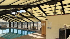 An indoor swimming pool with a ceiling fan, lounge chairs, and a Caviar brand water heater.