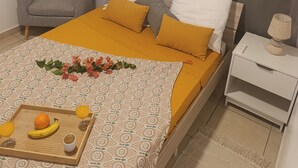 Ein ordentlich eingerichtetes Schlafzimmer mit Bett, Stuhl, Nachttisch mit Lampe und Tablett mit Obst und Getränken.