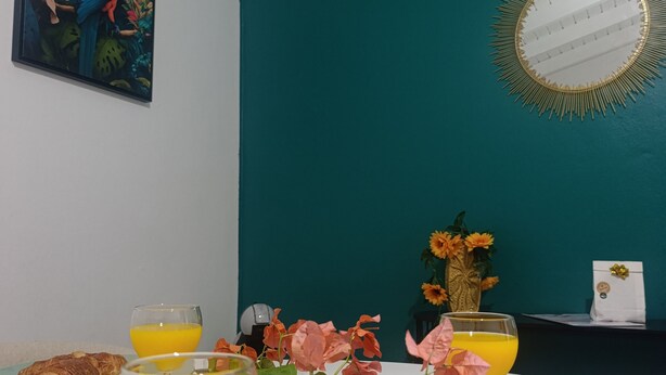 Ein Esstisch mit Croissants, Orangensaft und Kaffee, eine Vase mit Blumen und ein Gemälde an der Wand.