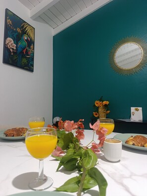 A breakfast table with croissants, orange juice, and coffee, a vase with flowers, and a painting on the wall. - Les hauts de Carrère, fleur-de-lys. (Petit-Bourg)