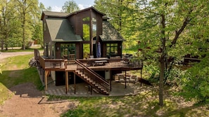Eine zweistöckige Holzhütte mit einer Terrasse, Sitzgelegenheiten im Freien und einer Treppe.