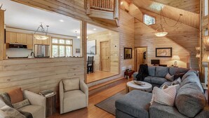 A spacious living area with a high ceiling, wooden walls, a cozy sofa, and a dining area with natural light. - Private Whitefish Chain Family Retreat on Little Pine Lake - Sleeps 10 (Crosslake)