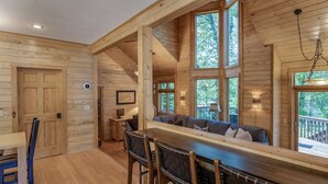 A wooden cabin interior with a bar area, seating, and large windows.