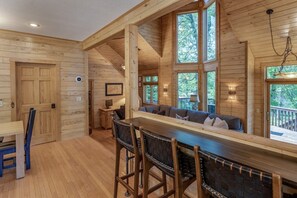 Interior de una cabaña de madera con barra, asientos y ventanas amplias.