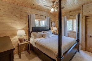 Ein Himmelbett mit Kopfteil, ein Nachttisch mit Lampe und ein Fenster mit Vorhängen.
