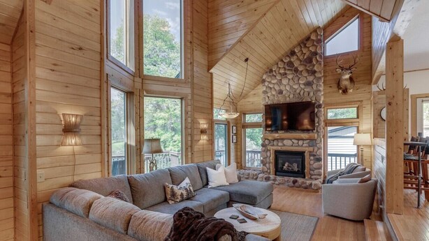 A log cabin interior with a large sectional sofa, stone fireplace, and large windows. - Private Whitefish Chain Family Retreat on Little Pine Lake - Sleeps 10 (Crosslake)