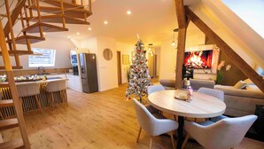 Ein modernes Loft mit einer Holztreppe, einem Essbereich mit rundem Tisch und Stühlen, einer Küche mit Kühlschrank sowie einem Wohnbereich mit Sofa und Kamin.