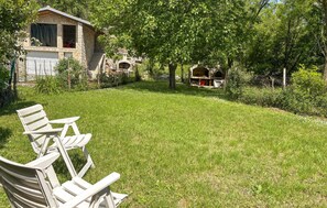 Un bâtiment en pierre doté d’un porche abrité, d’une cour verdoyante et d’une rangée de chaises blanches.