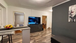 Una sala de estar moderna con un televisor de pantalla plana, un comedor con un taburete de bar y un sofá gris.
