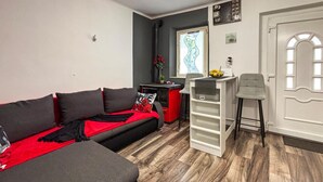 Un espacio habitable compacto con sofá, kitchenette pequeño, una puerta blanca y una ventana con vistas.