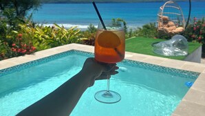 A hand holding a glass with a drink by a pool with a view of the sea and mountains. - Beachfront villa in Samaná with private pool (Las Galeras)