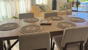 A dining area with a table set for six, surrounded by chairs, a sofa, and a view of the ocean through a sliding glass door. - Beachfront villa in Samaná with private pool (Las Galeras)