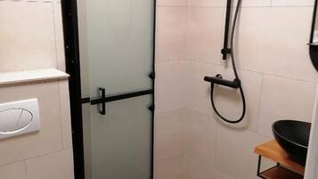 A small bathroom with a toilet, a glass shower enclosure, and a sink with a black basin.