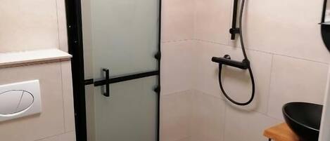 Une petite salle de bain comprenant des toilettes, une douche en verre et un lavabo avec un receveur noir.