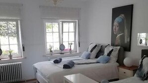 A bedroom with two beds, a bedside table, a radiator, and a window with curtains. - Le Domaine d'Eva (Libramont-Chevigny)