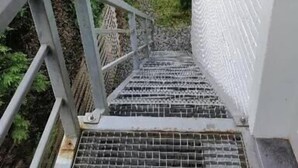 A metal staircase leading to a white brick wall, surrounded by greenery. - Le Domaine d'Eva (Libramont-Chevigny)