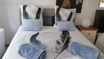 Uma cama com um quadro de uma mulher, almofadas com desenhos de penas e a inscrição 'Douceur de plumes' no cobreleito.