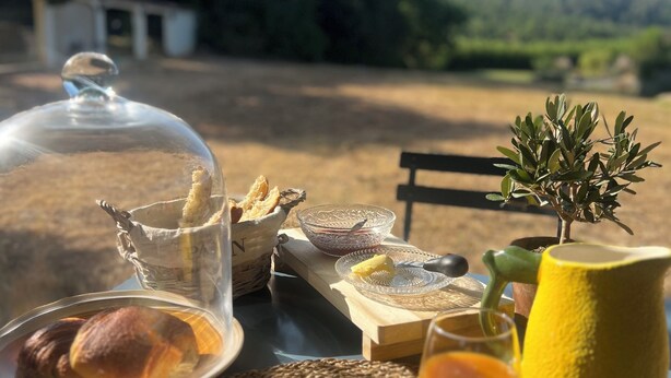 En frukostuppsättning med bröd, smör, kaffe och en kanna med citron på ett bord utomhus.
