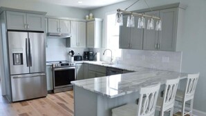 A modern kitchen with stainless steel appliances, a marble island, and white bar stools. - Coastal Retreat Near Beaufort (Beaufort)
