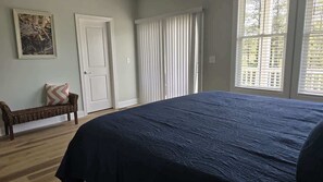 A bedroom with a large bed, a bench, a door, and a window with blinds. - Coastal Retreat Near Beaufort (Beaufort)