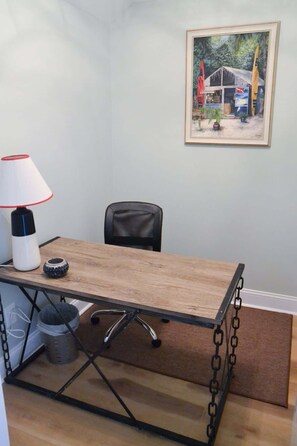 A small office space with a wooden desk, a chair, a lamp, a trash bin, and a framed painting on the wall. - Coastal Retreat Near Beaufort (Beaufort)