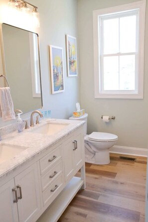 A bathroom with a white vanity, a large mirror, a toilet, and a window. - Coastal Retreat Near Beaufort (Beaufort)