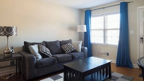 Una sala de estar con sofá, mesa de centro, lámpara y ventana con cortinas.