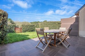 Un patio con mesa y sillas de madera, rodeado por un seto y una valla de madera.