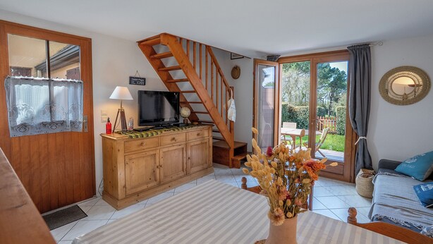 Ein gemütliches Wohnzimmer mit einer Holztreppe, einem Fernseher und einem Essbereich mit Tisch und Stühlen.