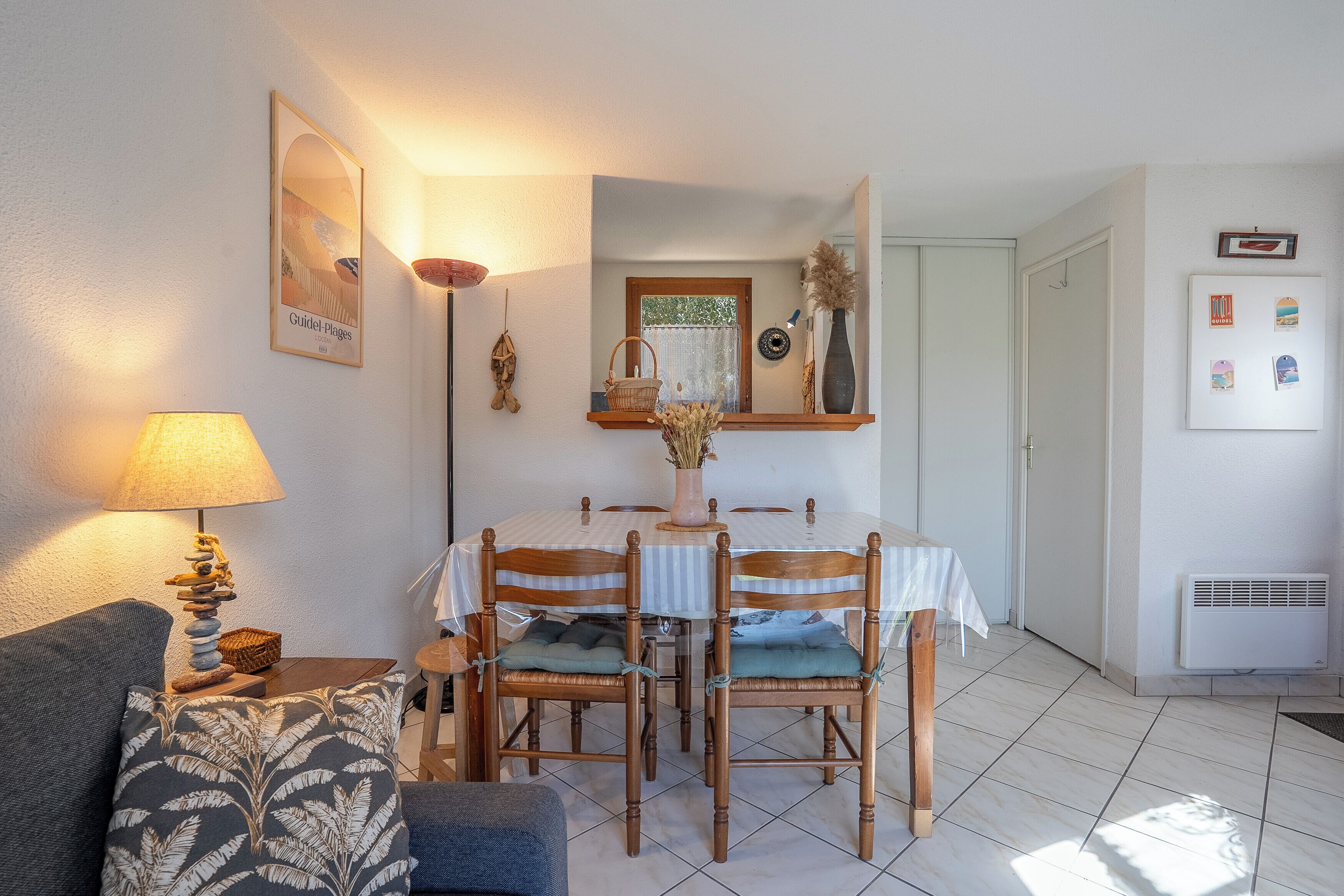 A dining area with a table and chairs, a lamp, a couch, and a wall-mounted shelf with decorative items.