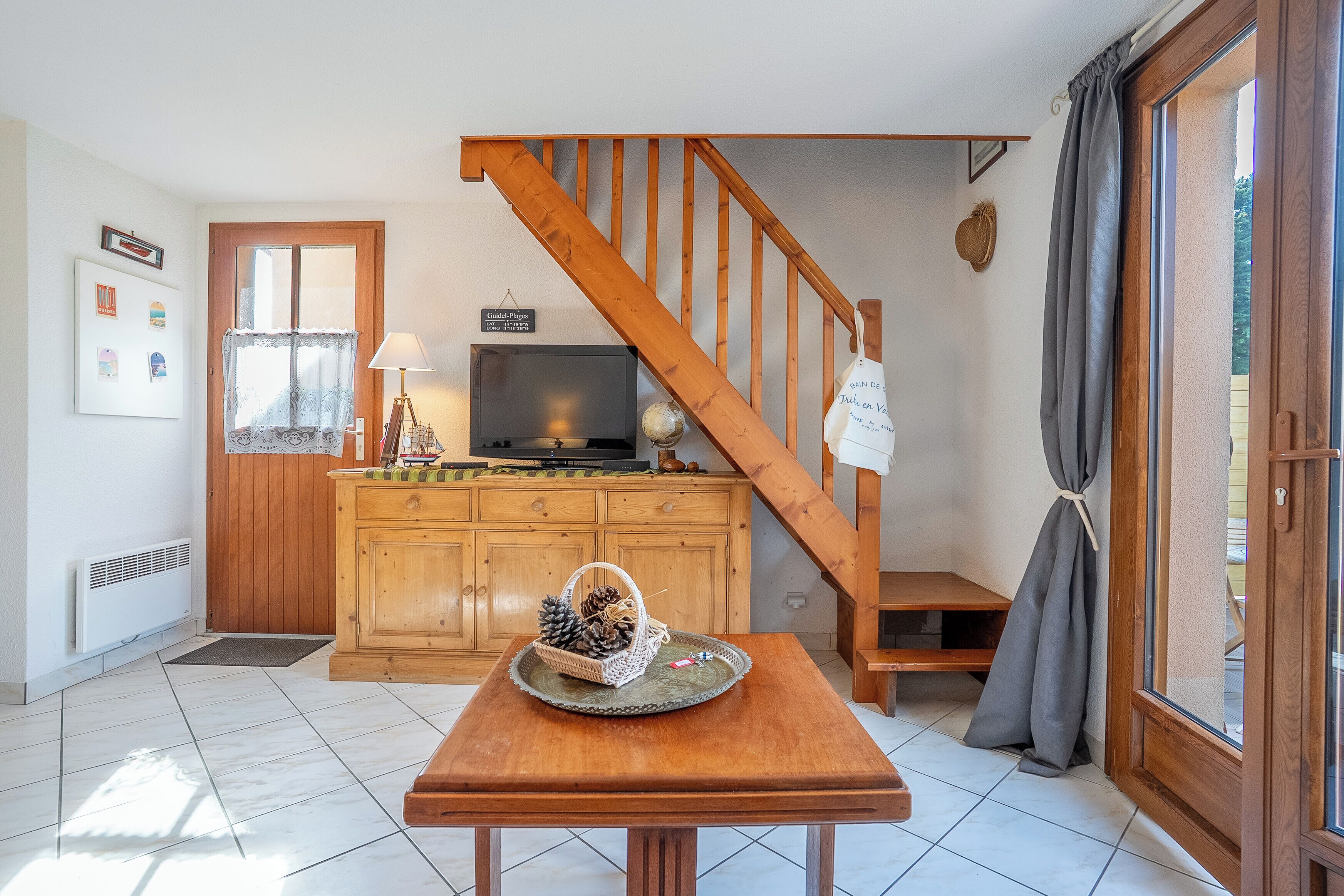 A kitchen with a wooden staircase, a television, and a basket with pinecones on a table.