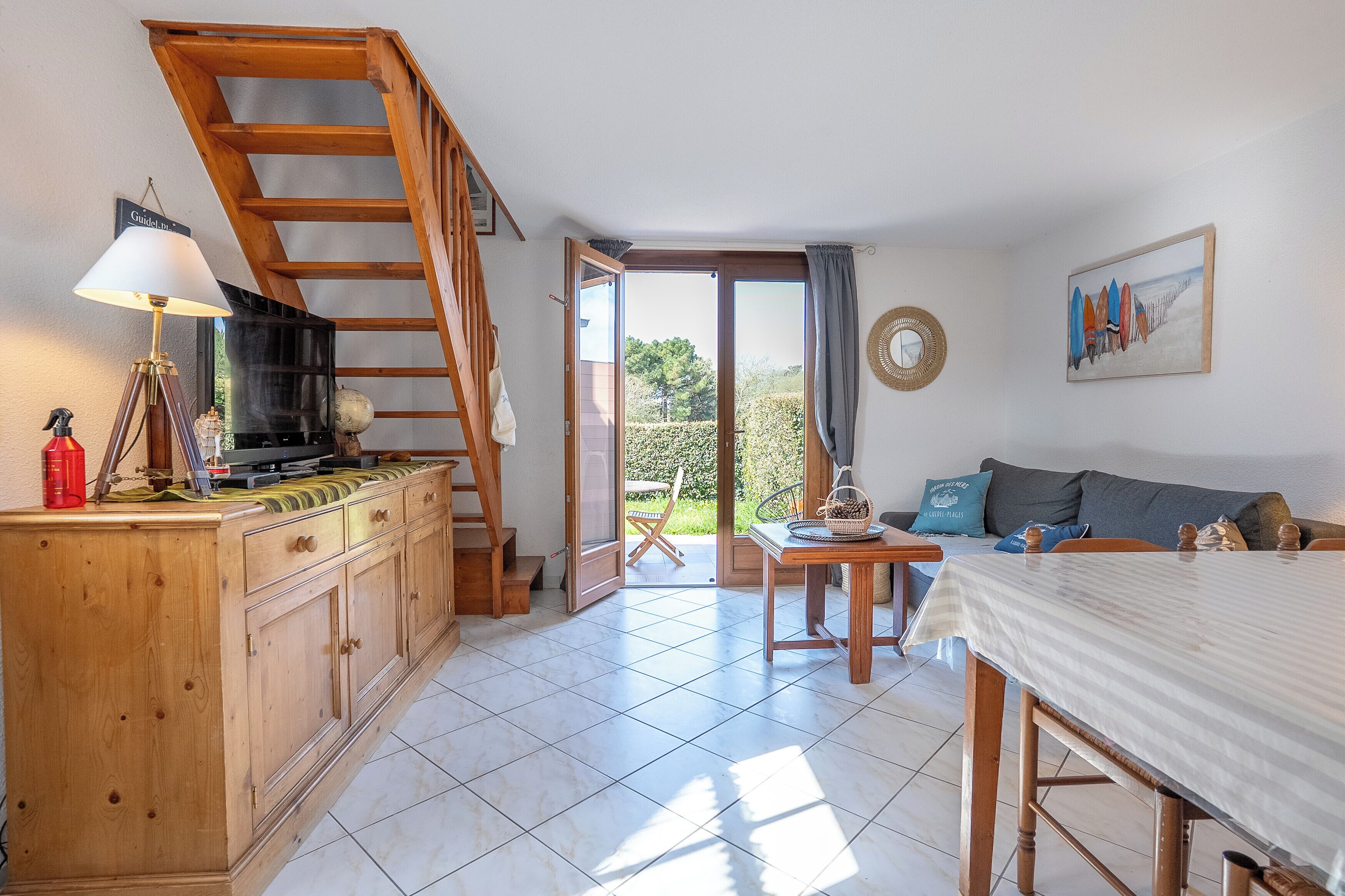 A room with a wooden staircase, a dining table, a sofa, and a view of the outdoors.