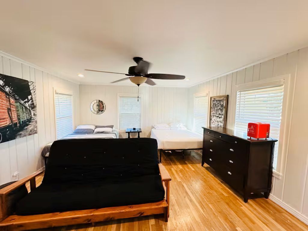 A bedroom with a bed, a desk, a dresser, a ceiling fan, and a window with blinds.