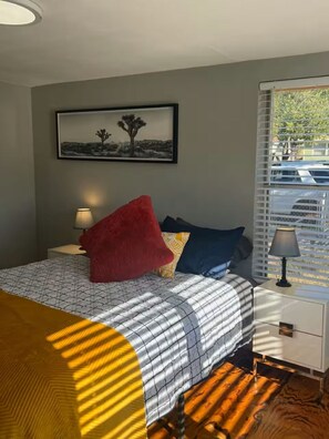 A bedroom with a bed, a nightstand, a lamp, a window with blinds, and a framed picture on the wall. - Perfect for 2: Pet Friendly (San Angelo)