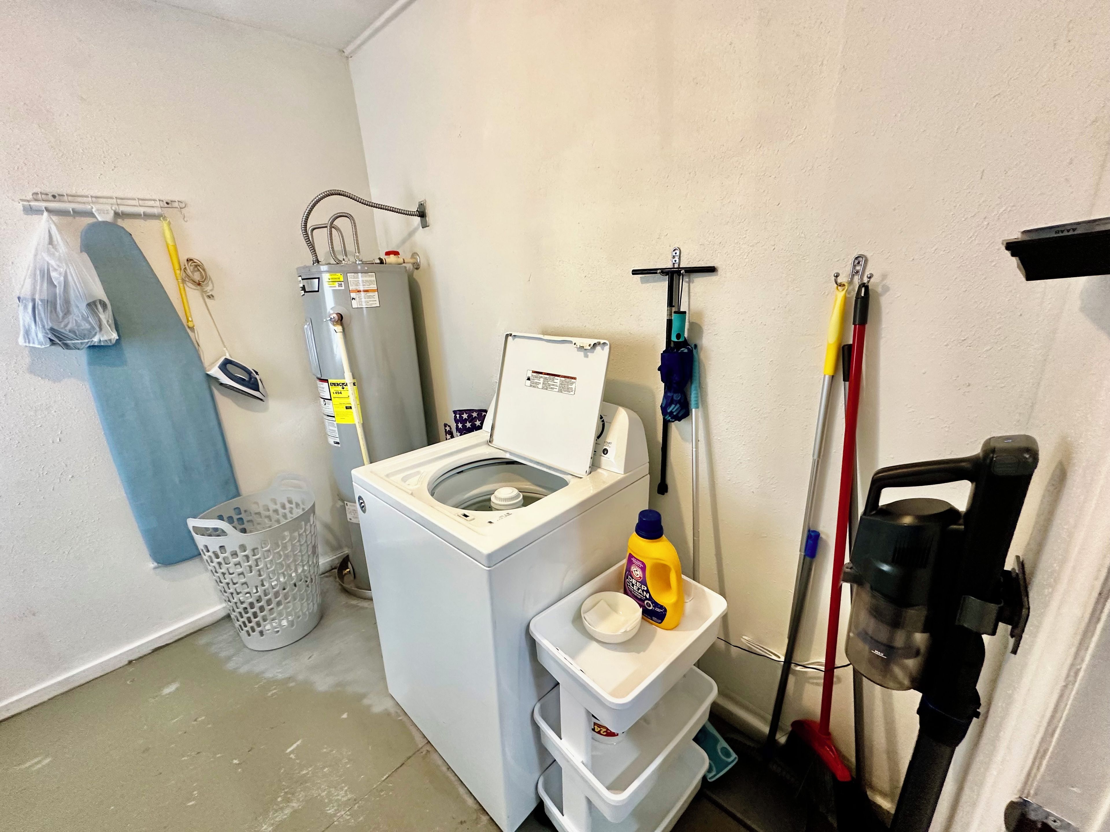 A laundry room with a washing machine, a water heater, and cleaning supplies.