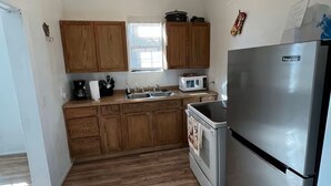 A compact kitchen with wooden cabinets, a stainless steel refrigerator, a microwave, and a stove. - Sleeps 4/ Fenced Yard/ Pet Friendly/ Near Downtown (San Angelo)