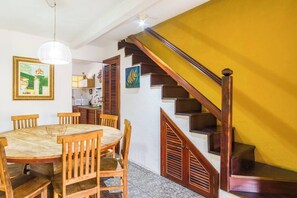 A dining area with a round table and wooden chairs, a staircase with wooden railings, and a kitchen area in the background. - Bromelia House, 15 minutes from the Historic Center (Paraty)