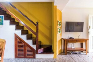 A staircase with wooden railings, a flat-screen TV mounted on the wall, and a wooden table with a power strip. - Bromelia House, 15 minutes from the Historic Center (Paraty)