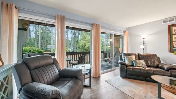A spacious living room with a leather sofa, a glass coffee table, and a balcony with outdoor furniture. - Birdie Bungalow - Sleeps 8 - Prime Location (Pinehurst)